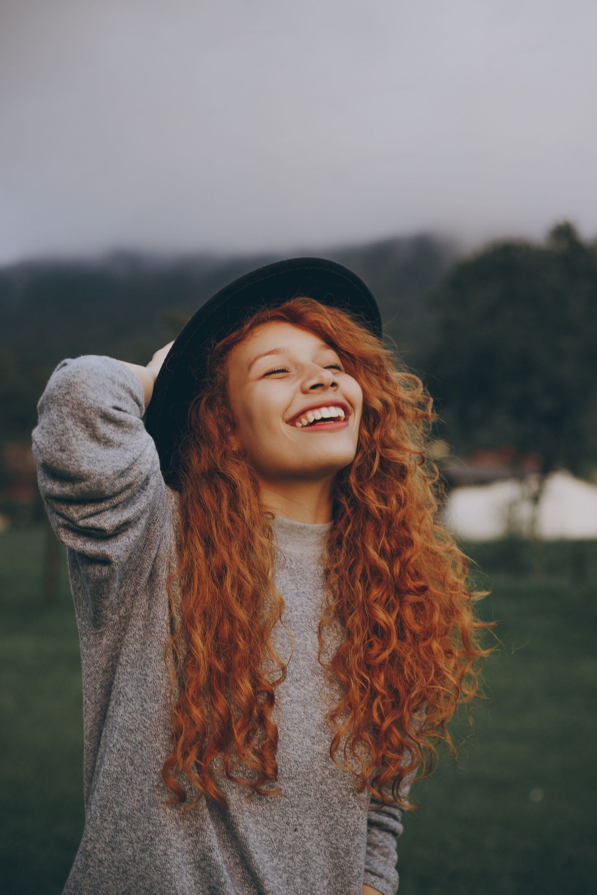 red headed woman with a hat on, looking up at the sky and smiling, with her eyes closed