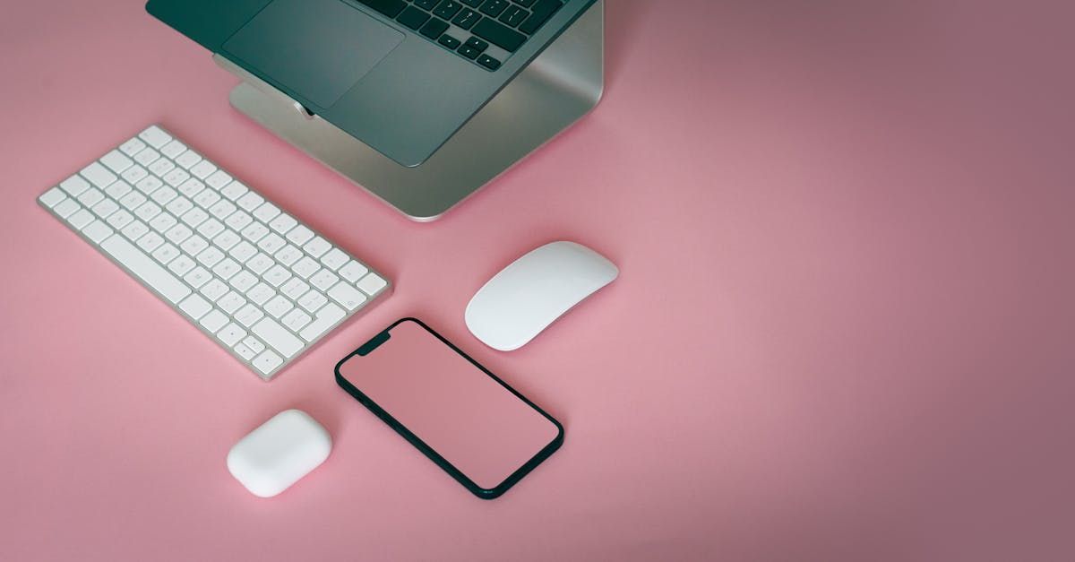 Laptop, keyboard, mouse, phone, and earbuds on a pink surface.