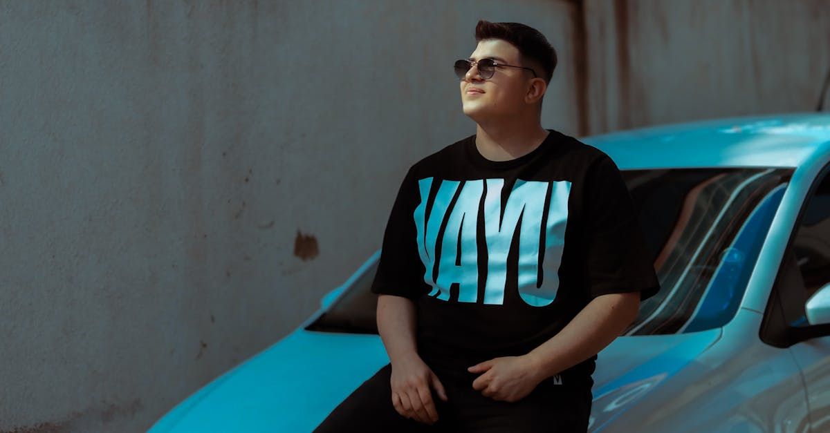 A man in a black t-shirt is sitting next to a blue car.