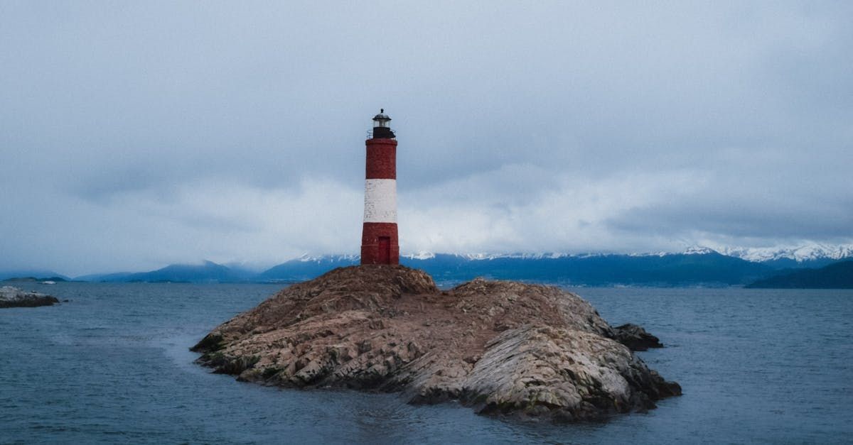 A red and white lighthouse is sitting on top of a small rock in the middle of the ocean.