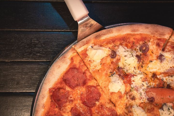 A pizza with pepperoni and cheese is sitting on a pan on a wooden table.