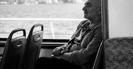 An elderly man is sitting on a bus looking out the window.