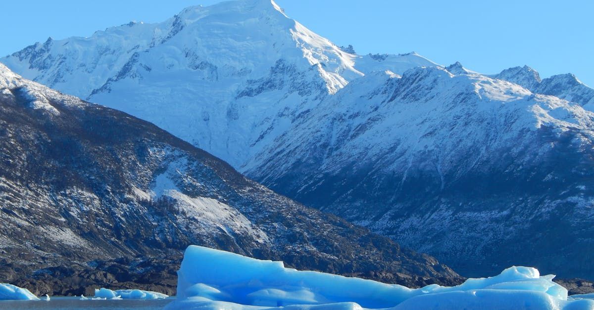 Un gran trozo de hielo azul flota frente a una montaña nevada.