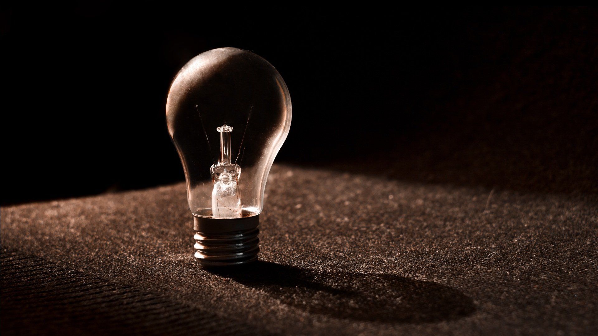 Lightbulb illuminated against a dark background, casting a shadow on a textured surface.