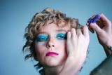 A woman with curly hair is getting her makeup done by a person.