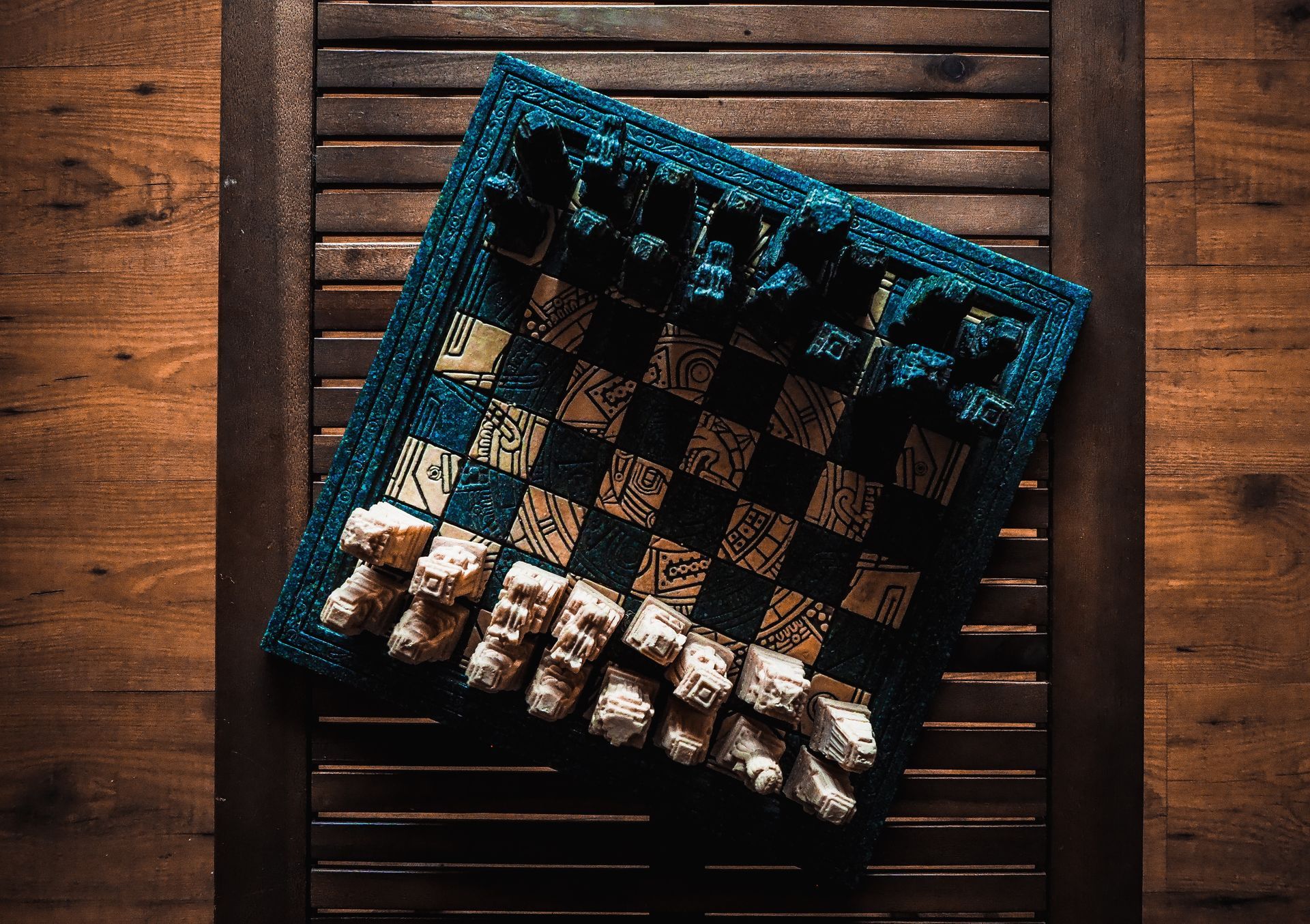 Chess set with turquoise border, tan and navy board, white pieces, on wooden shutters.