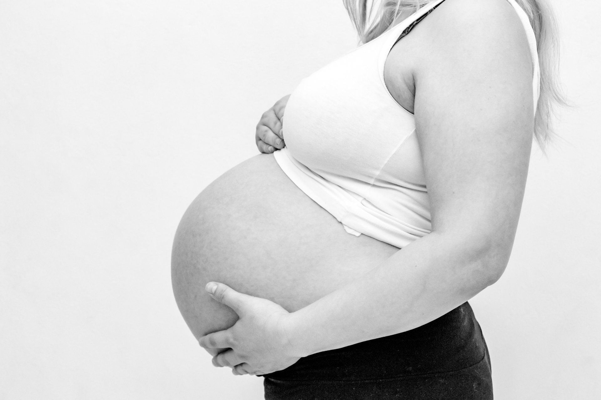 A pregnant woman is holding her belly in a black and white photo.