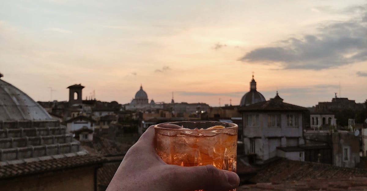 En person holder et glass iste foran en bysilhuett ved solnedgang.