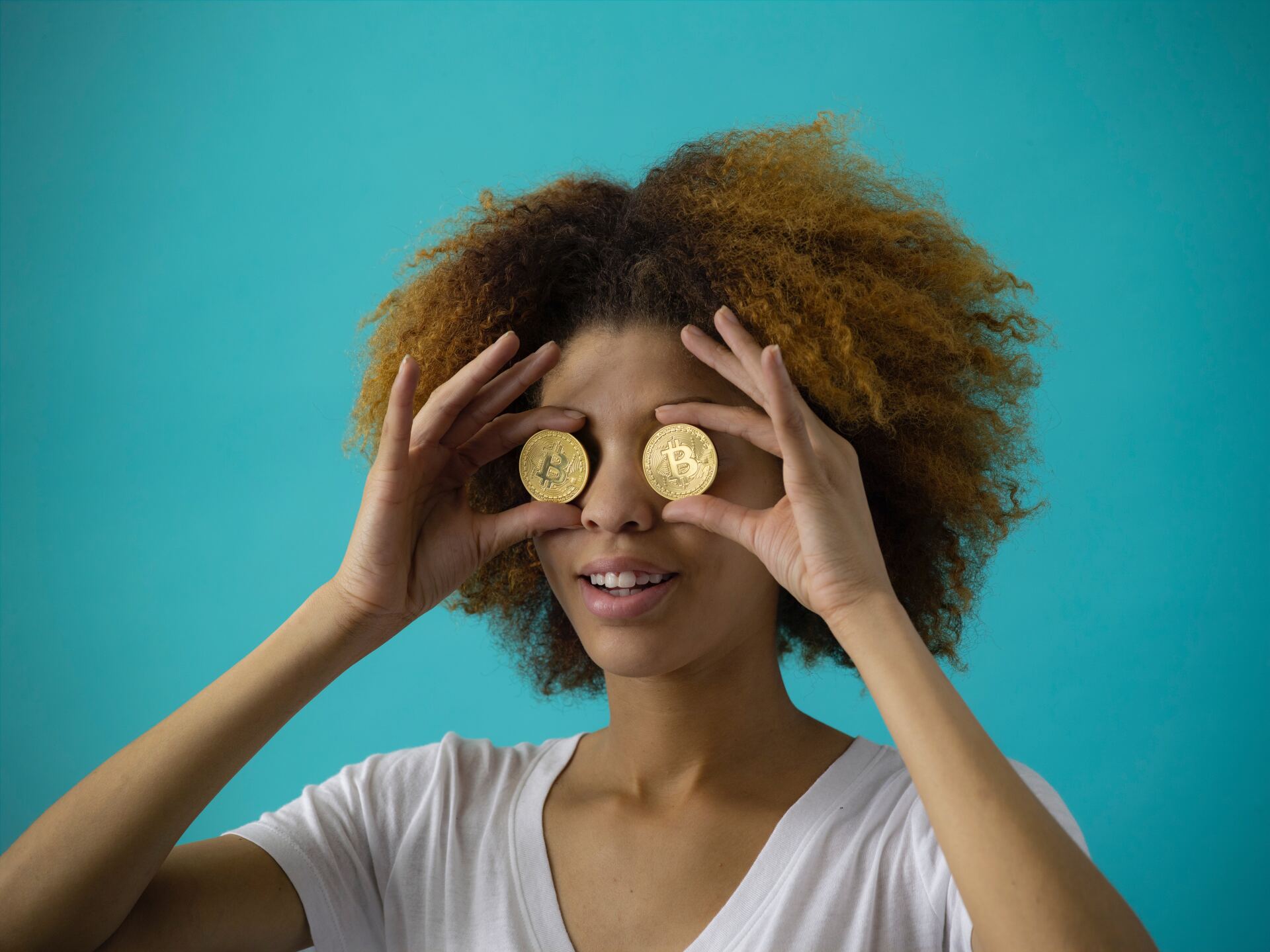 A lady is holding two BitCoin physical coins up against her eyes to show that she is looking for something