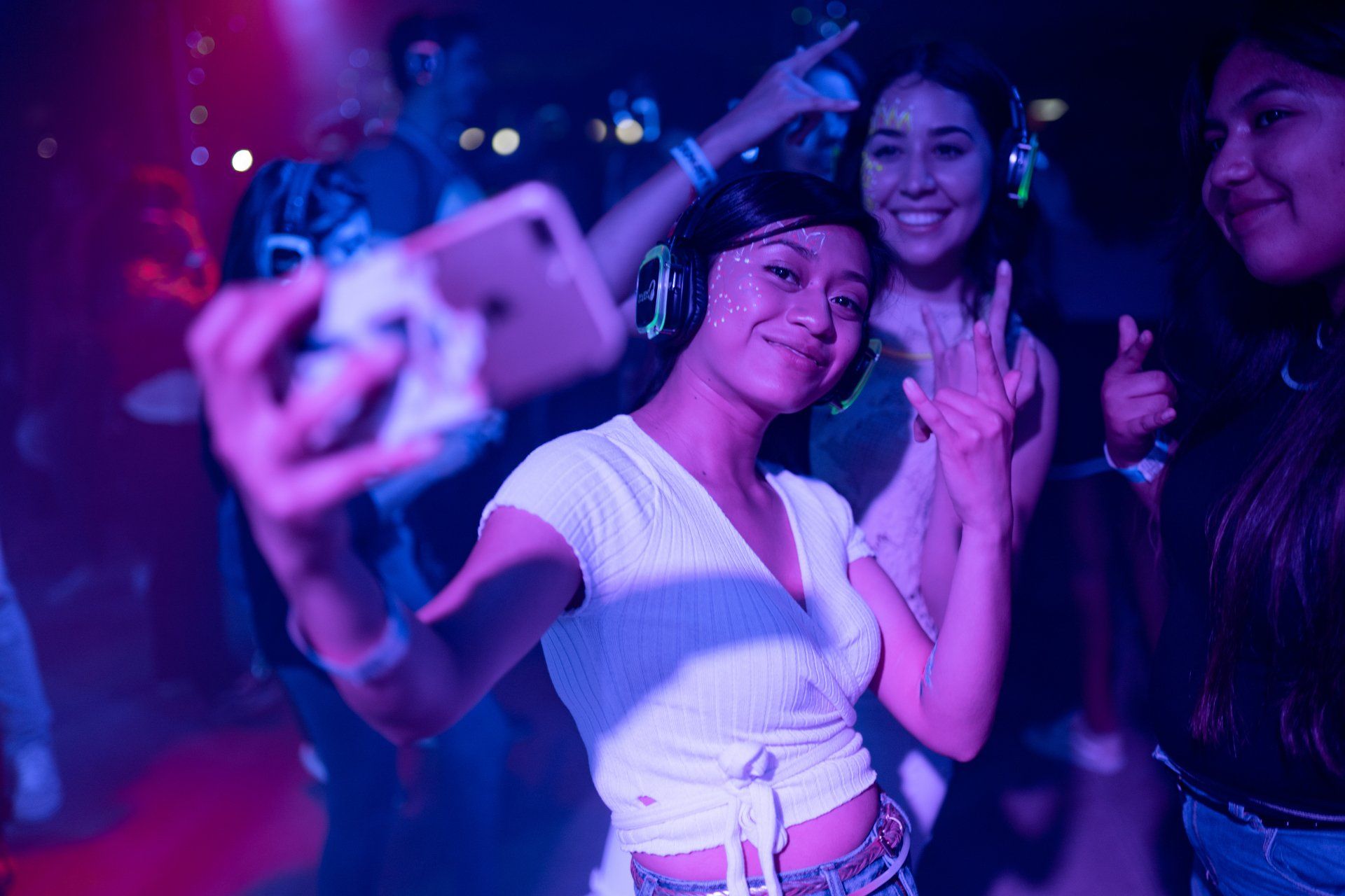 A woman is taking a selfie with her phone at a party.