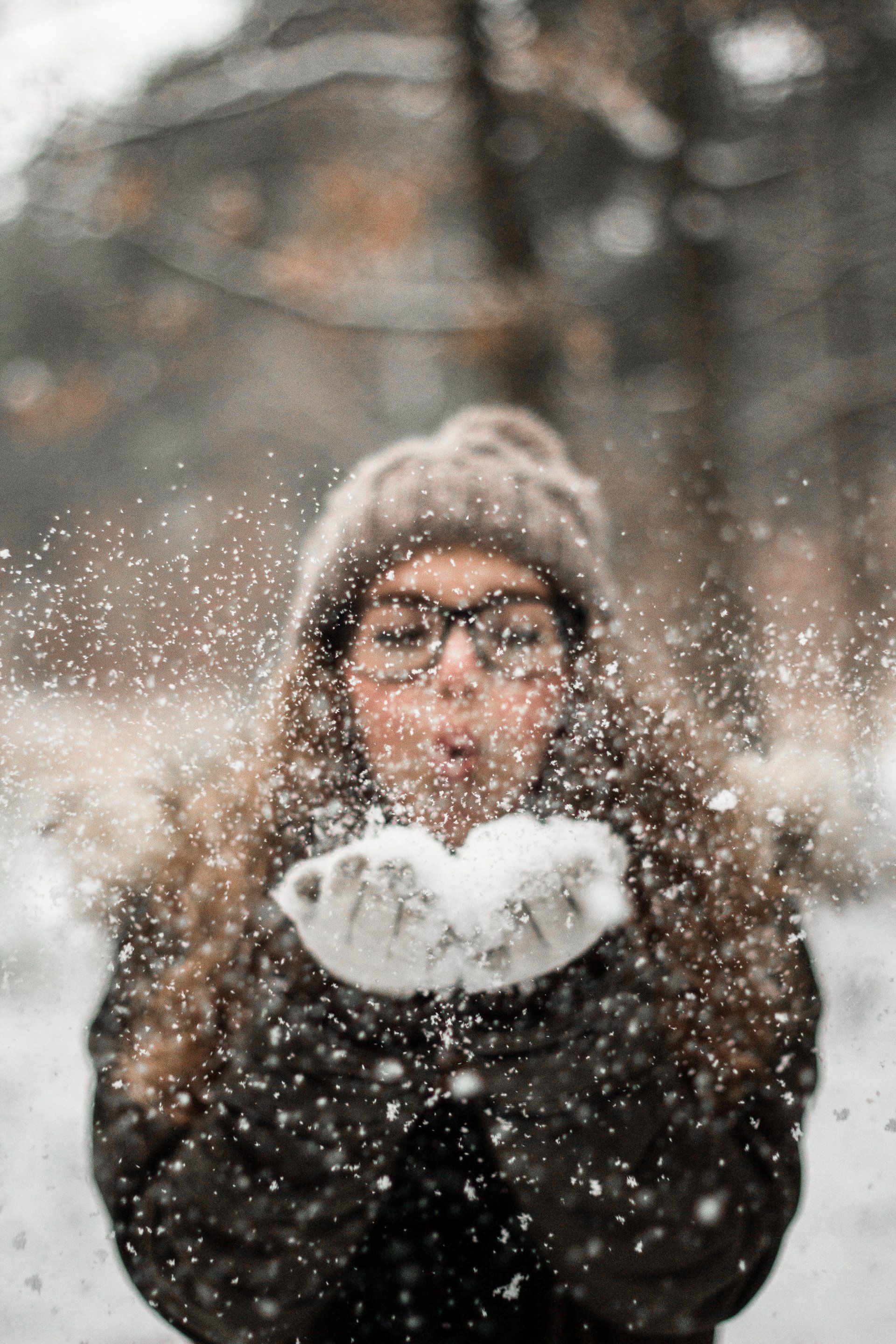 A woman is blowing snow from her hands in the air.