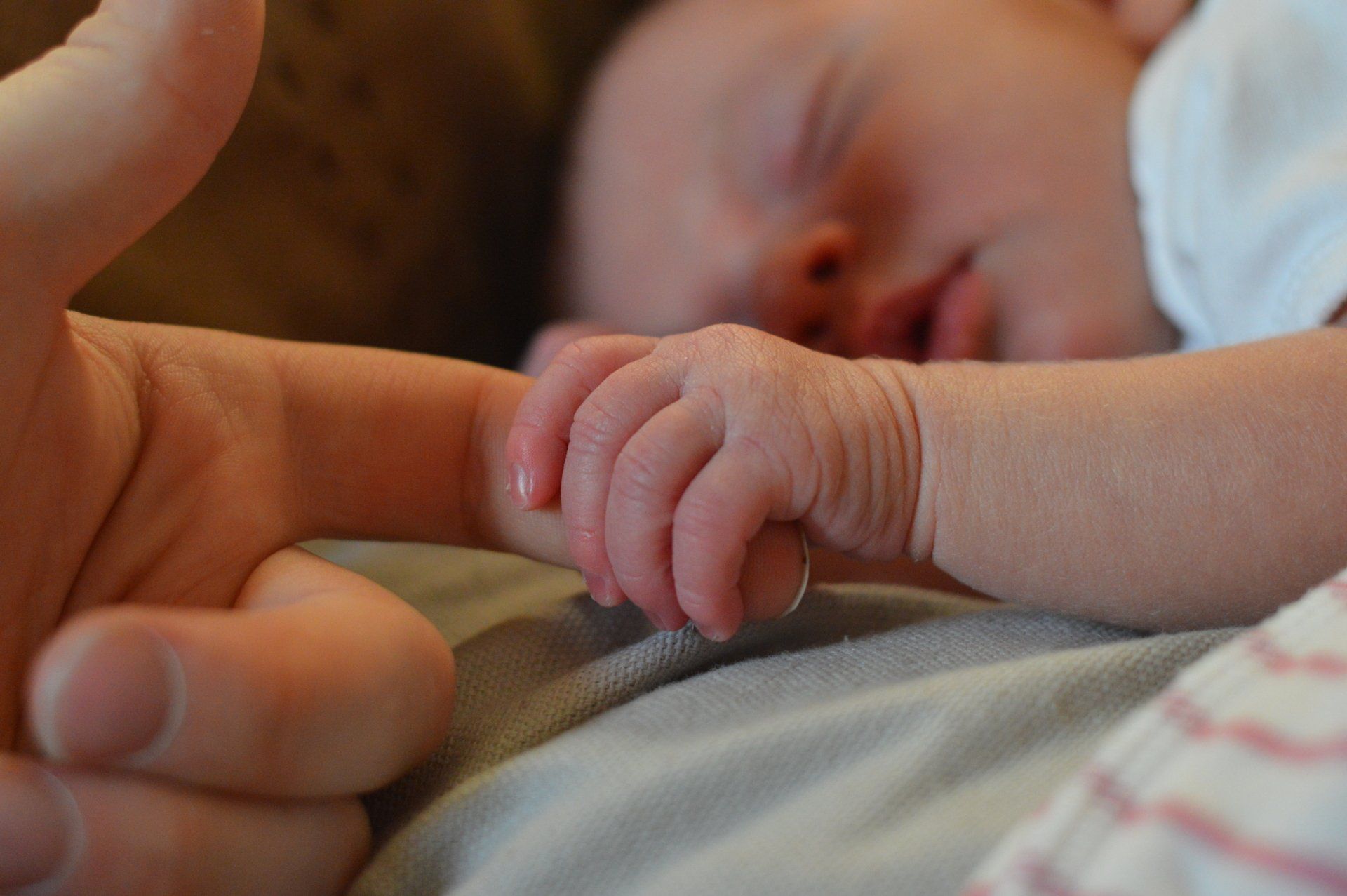Newborn baby holding adult finger