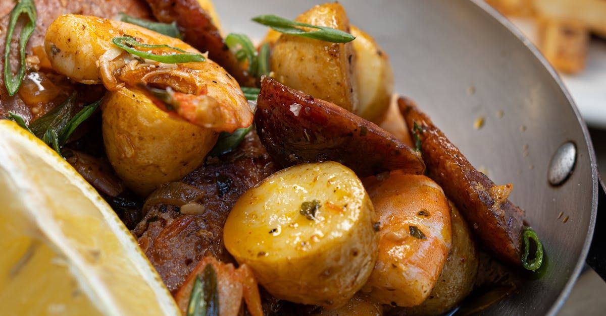 A close up of a pan filled with shrimp and potatoes with a slice of lemon.