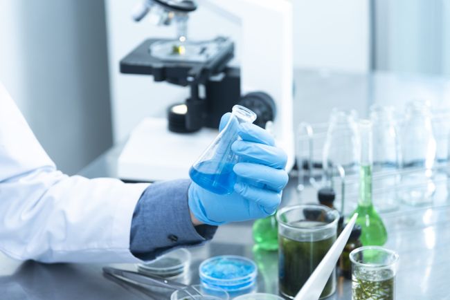 A scientist is holding a beaker of blue liquid in a laboratory.