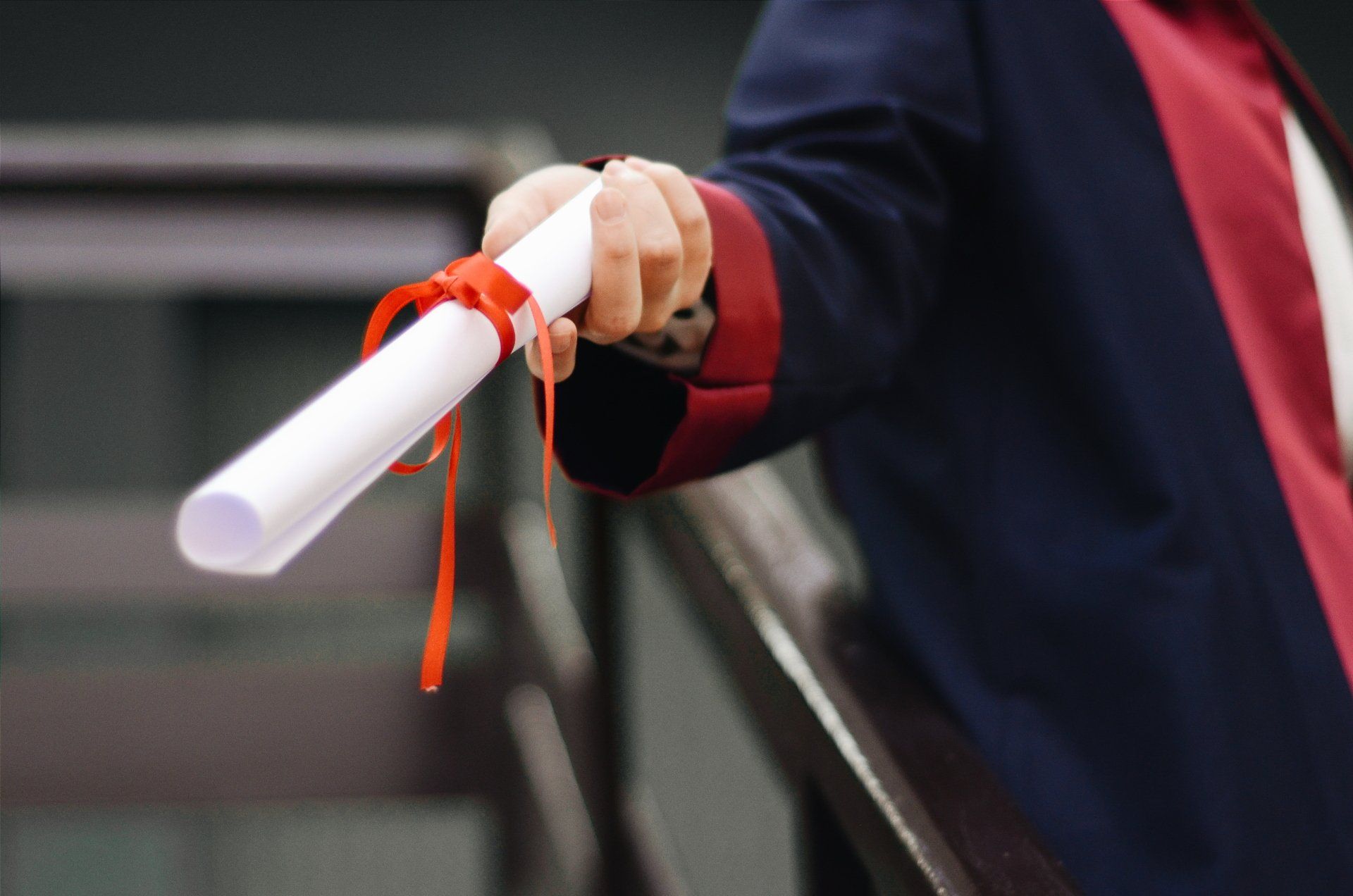 A person dressed in a graduation gown holding a diploma with a ribbon around it.
