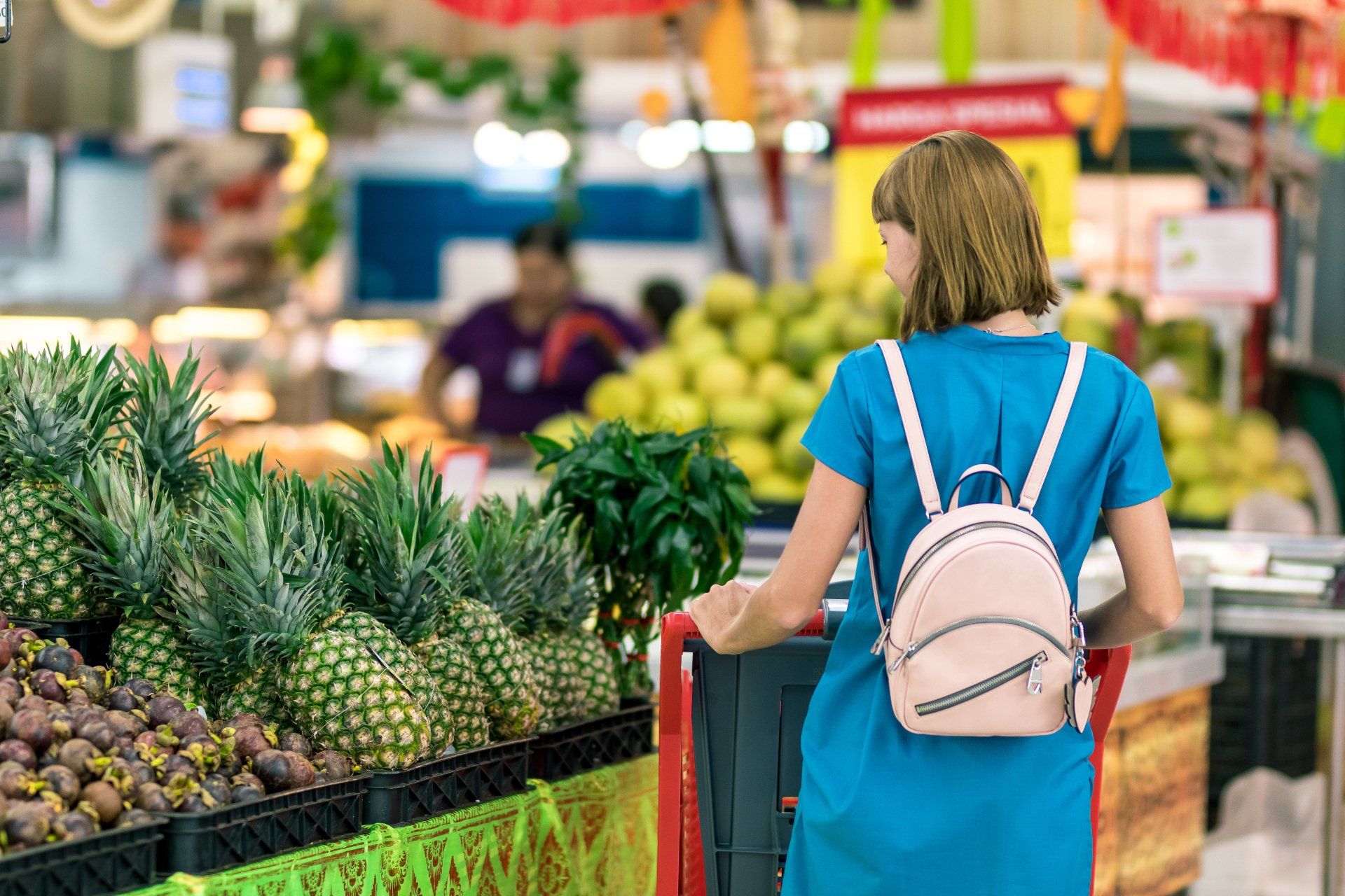 A woman with a backpack is pushing a shopping cart in a grocery store.