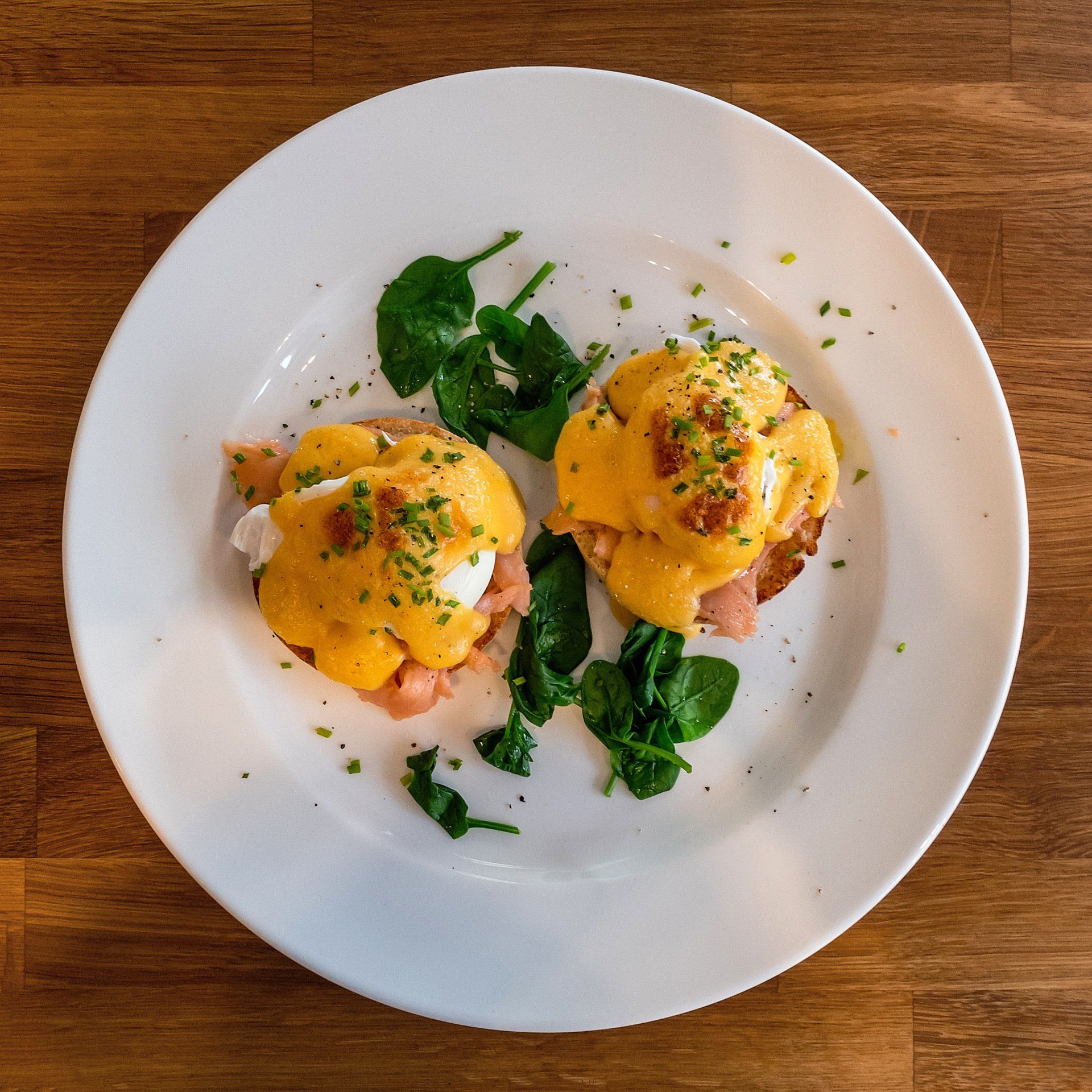 A white plate topped with eggs benedict and spinach on a wooden table.
