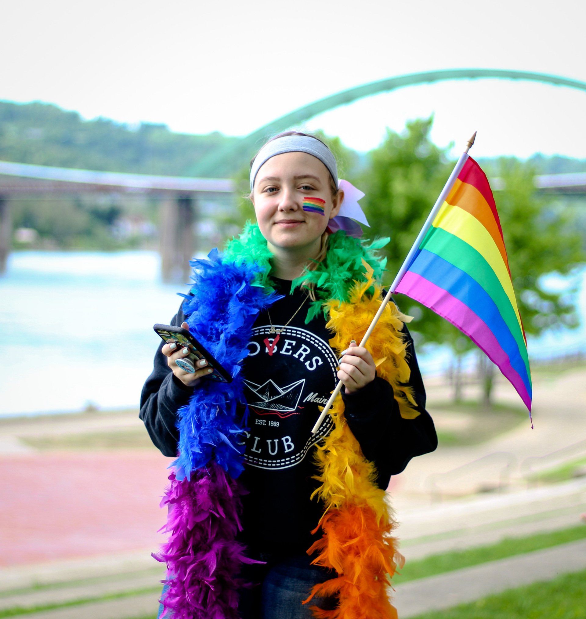 A woman wearing a rainbow boa and holding a rainbow flag