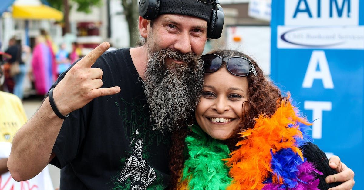 A man with a beard is posing for a picture with a woman in a colorful boa.