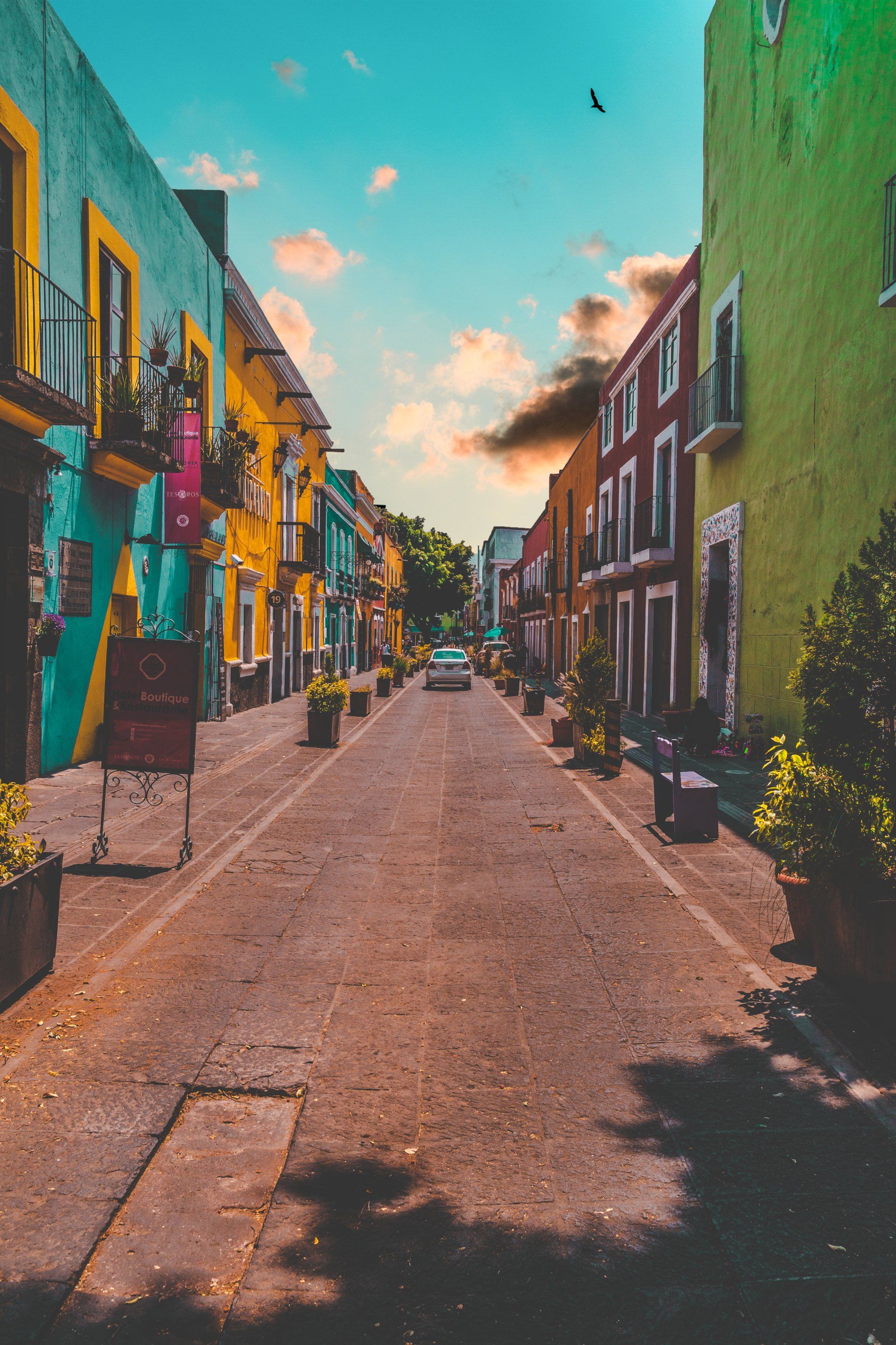 A car is driving down a narrow street lined with colorful buildings.