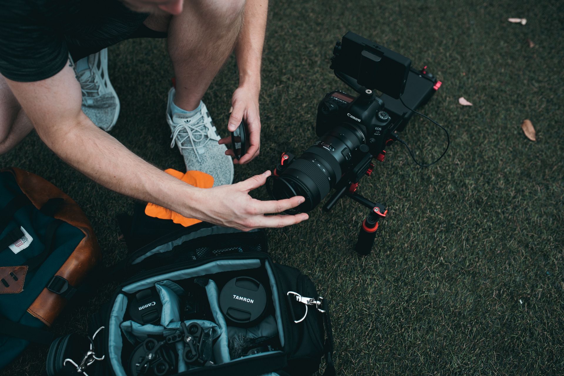 A man is kneeling down next to a camera and a backpack.