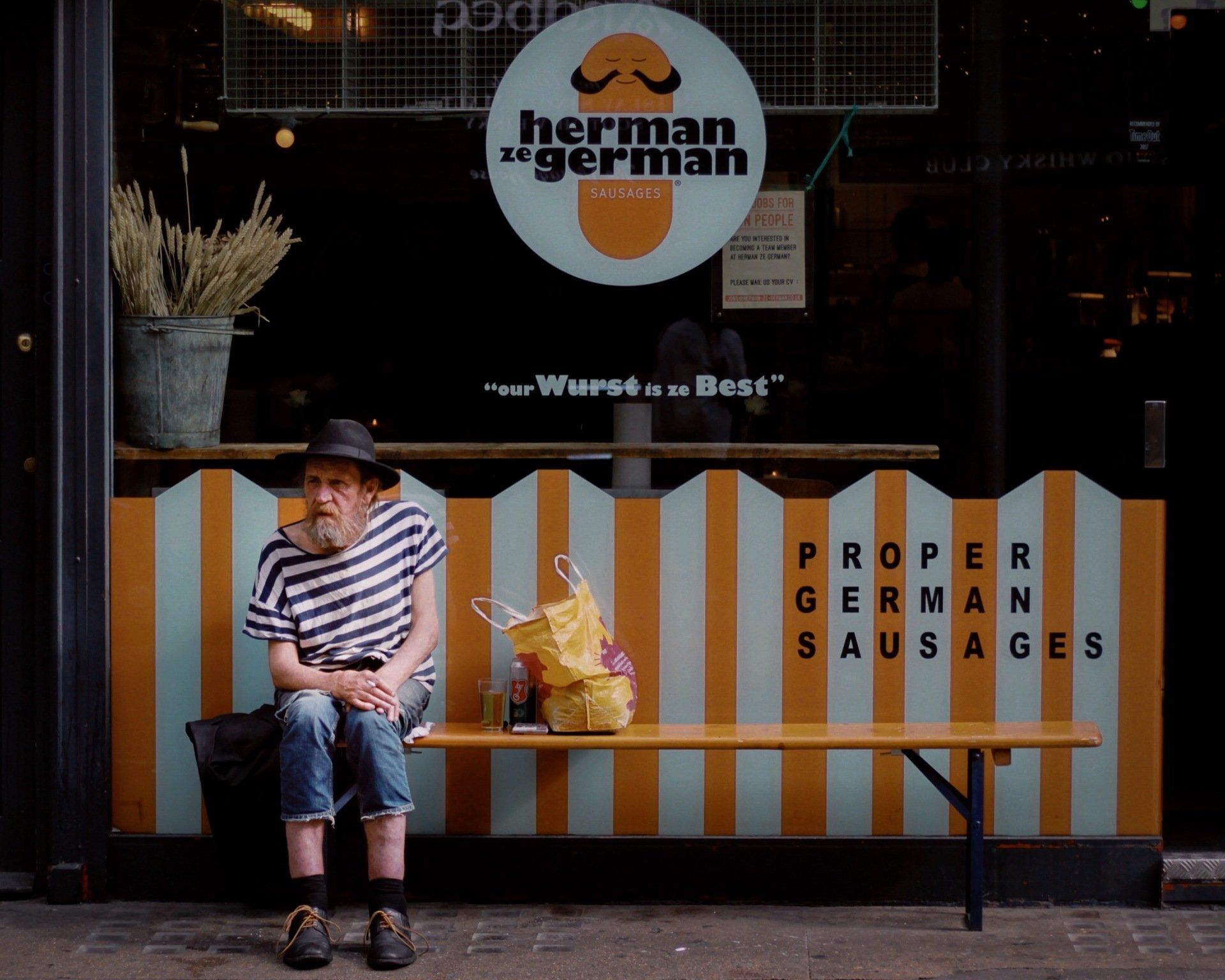 A man sits on a bench in front of a store that sells proper german sausages