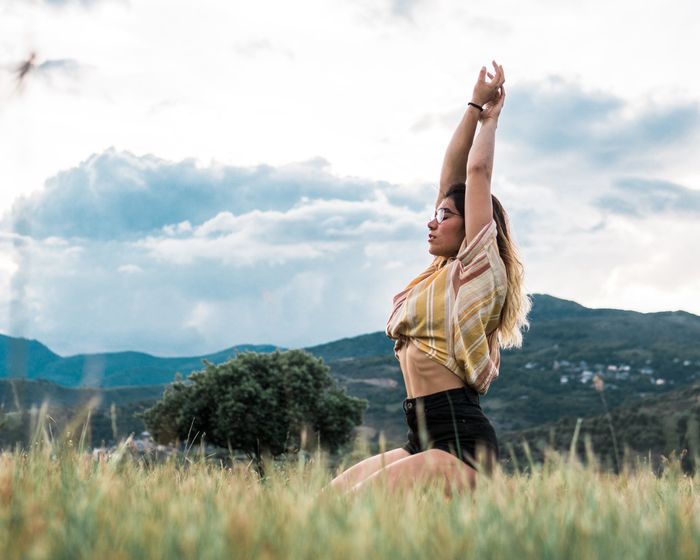 A woman is sitting in a field with her arms outstretched.