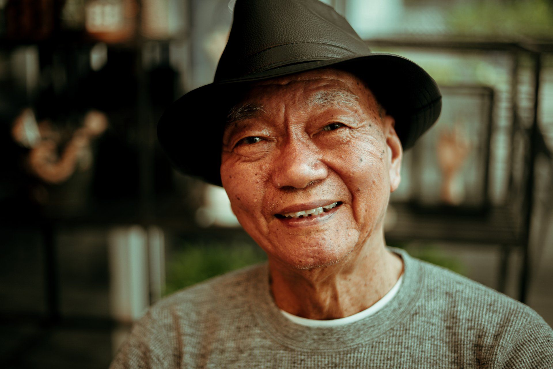 An elderly man wearing a hat and a sweater is smiling for the camera.