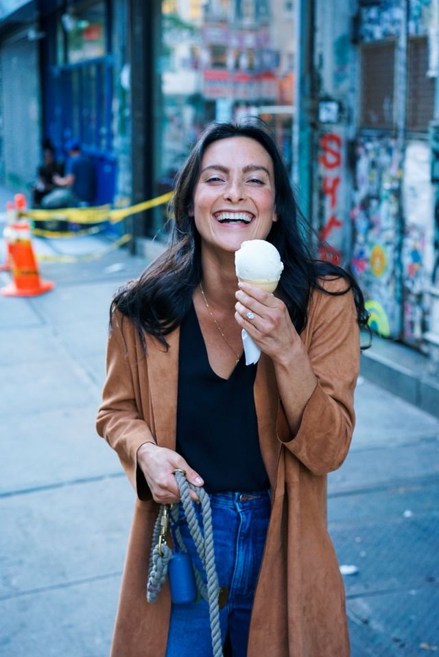 A woman is eating an ice cream cone on the sidewalk.