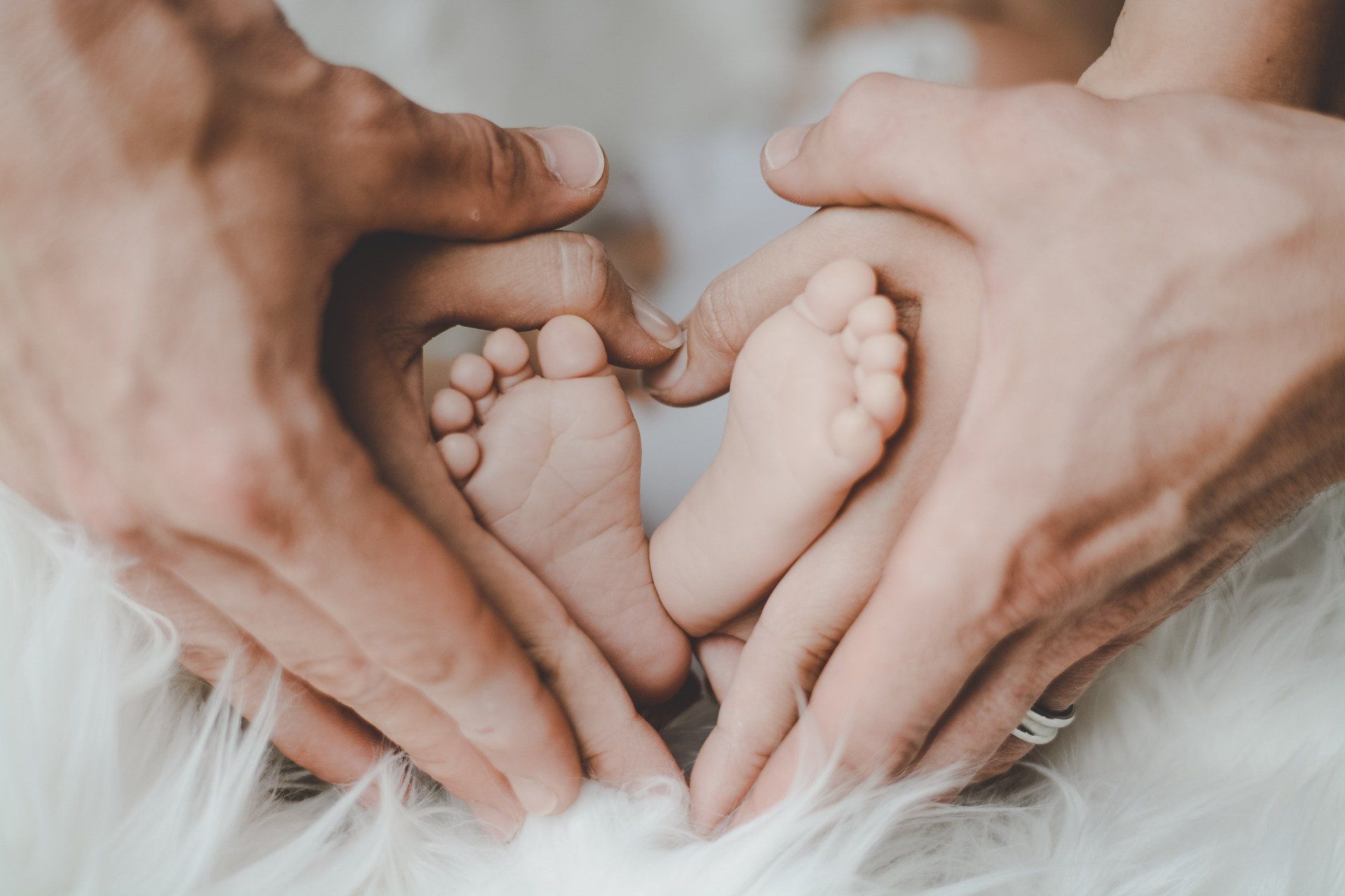 A family is making a heart shape with their hands around a baby 's feet.