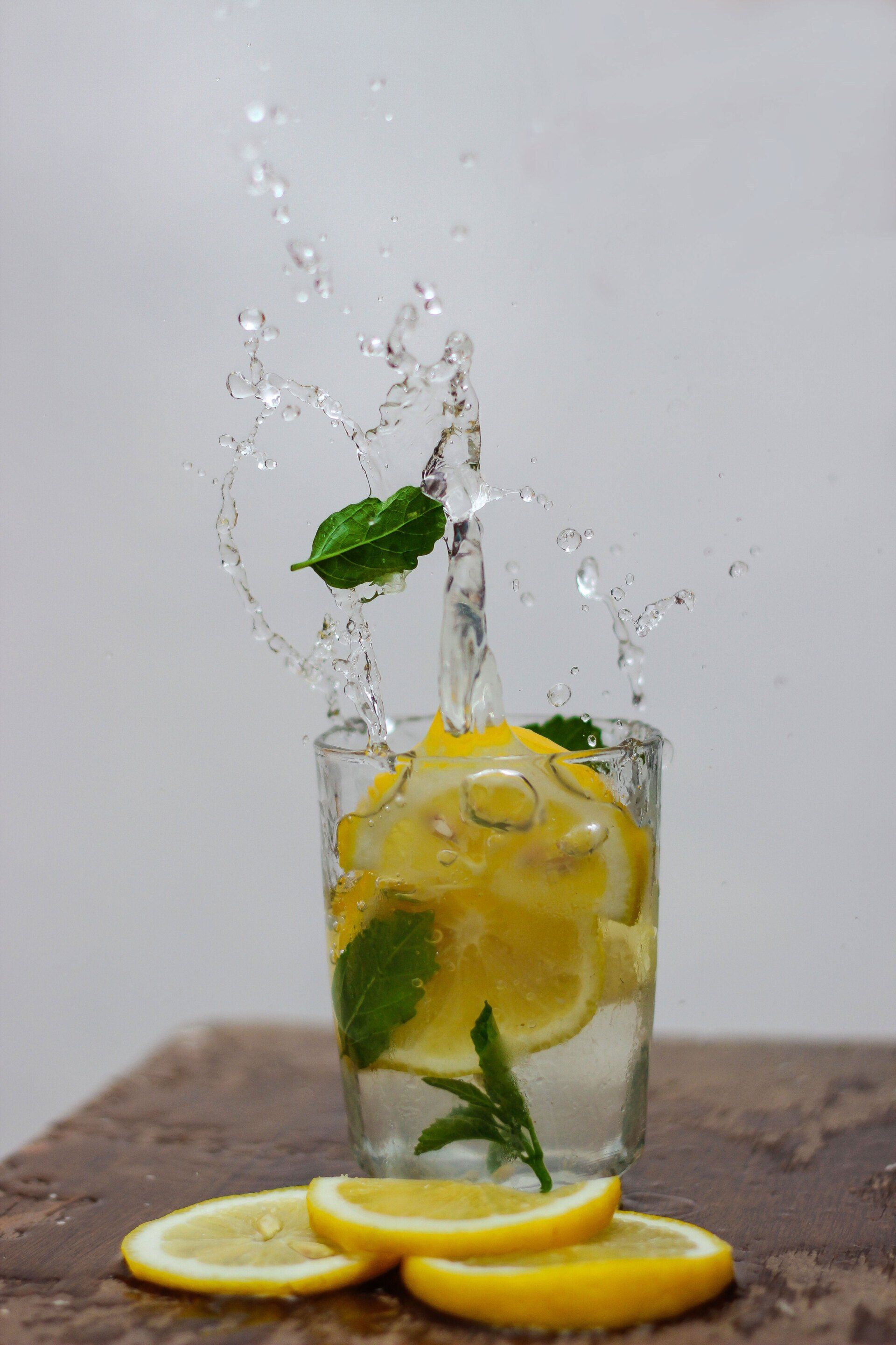 A glass of water with lemon slices and mint leaves splashing out of it.