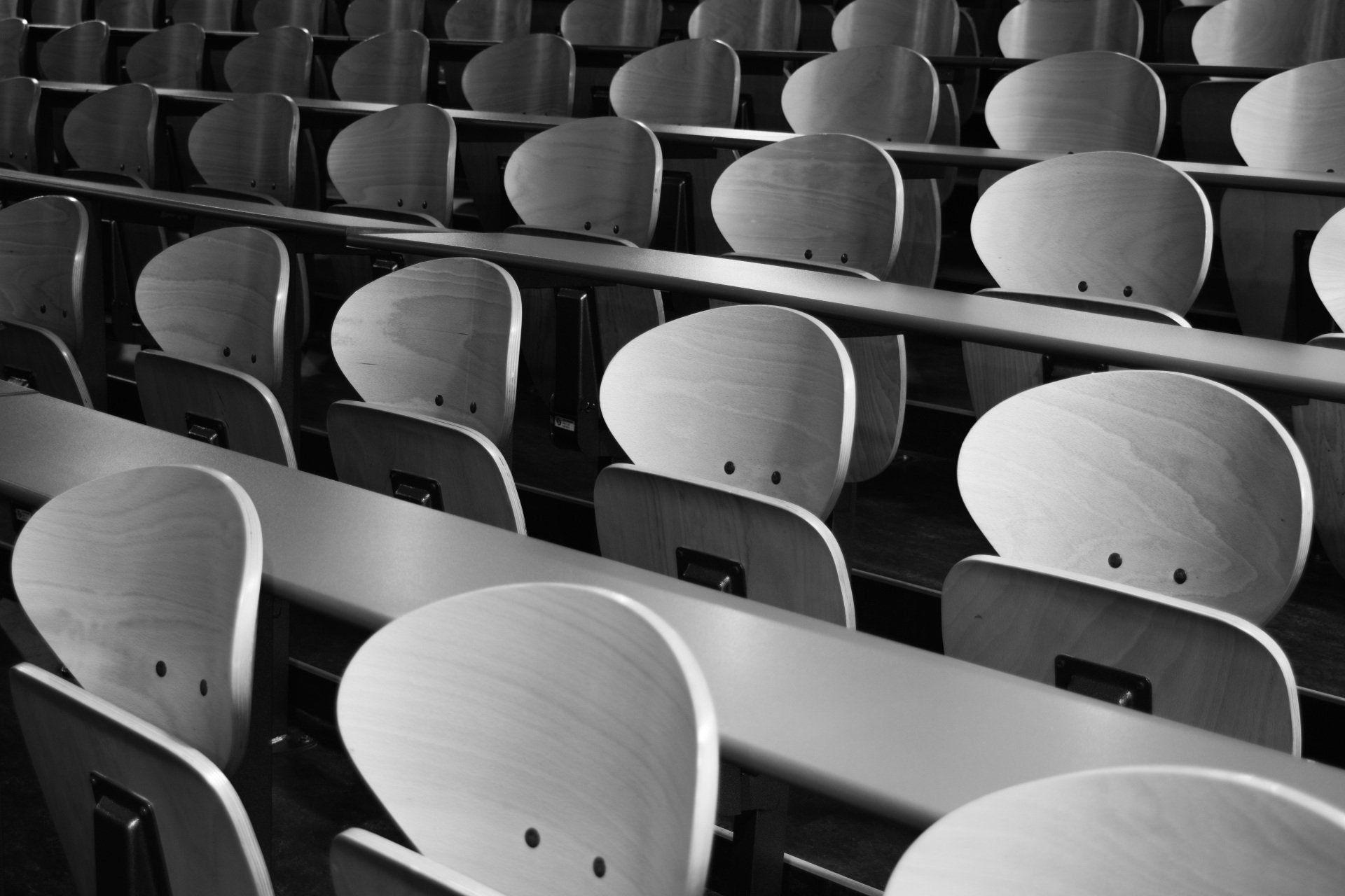 A black and white photo of rows of wooden chairs in an auditorium