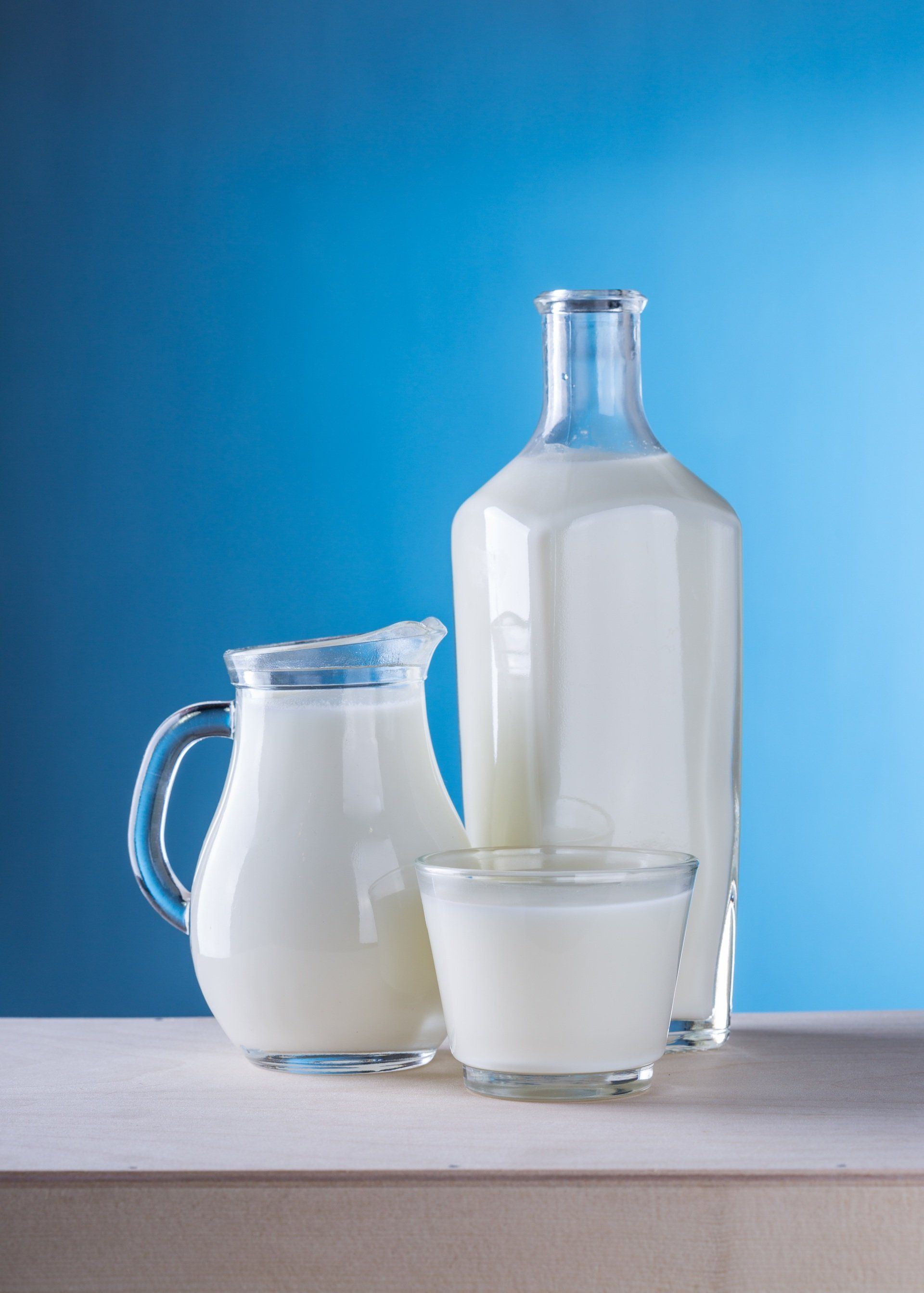 Uma garrafa de leite, uma jarra de leite e um copo de leite sobre uma mesa.