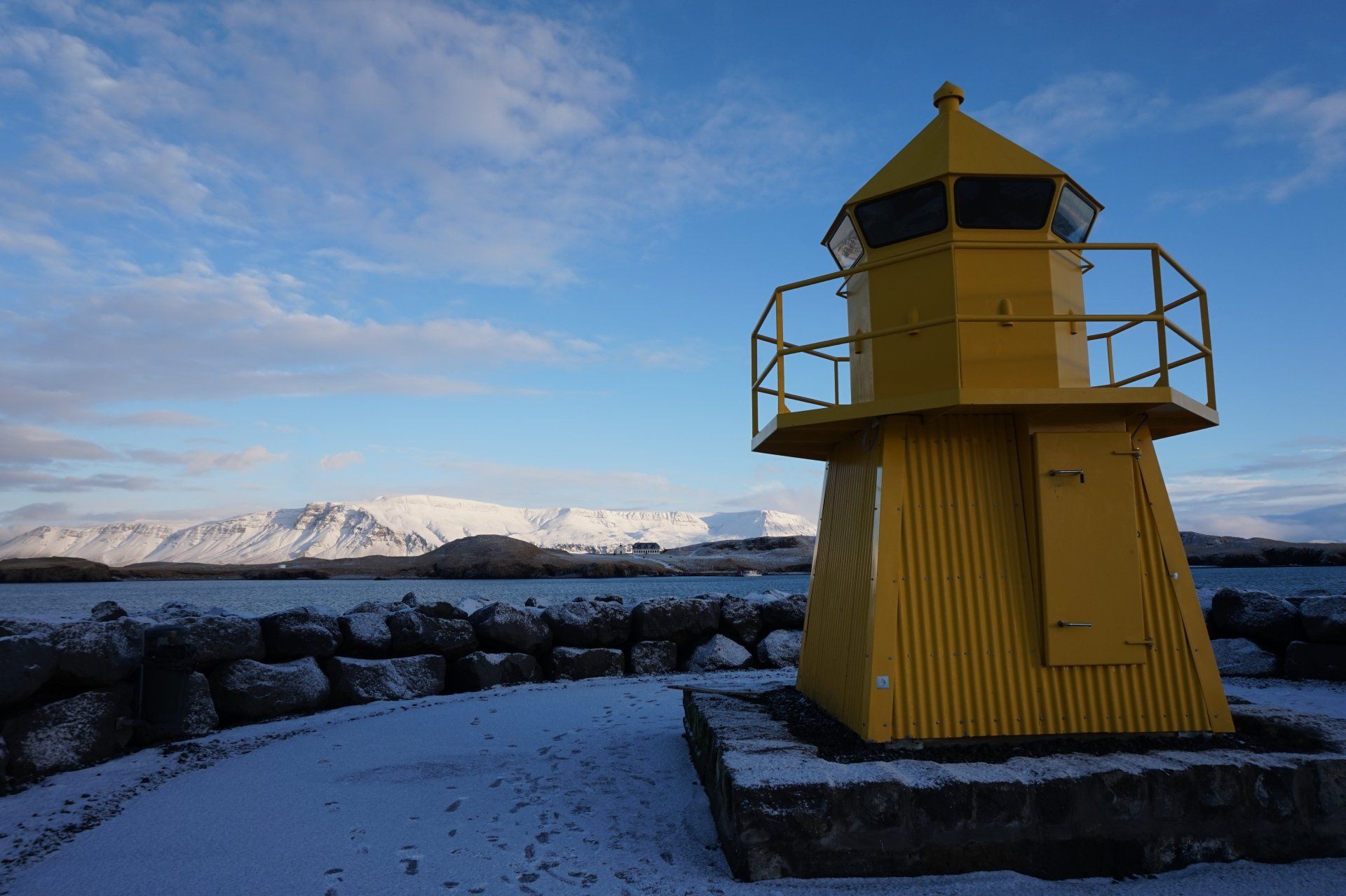 A yellow lighthouse in the snow with mountains in the background