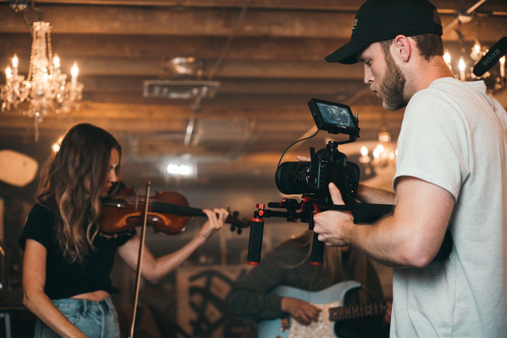 A man is holding a camera while a woman plays a violin.