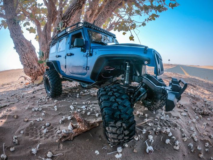 A blue jeep is parked in the sand near a tree.