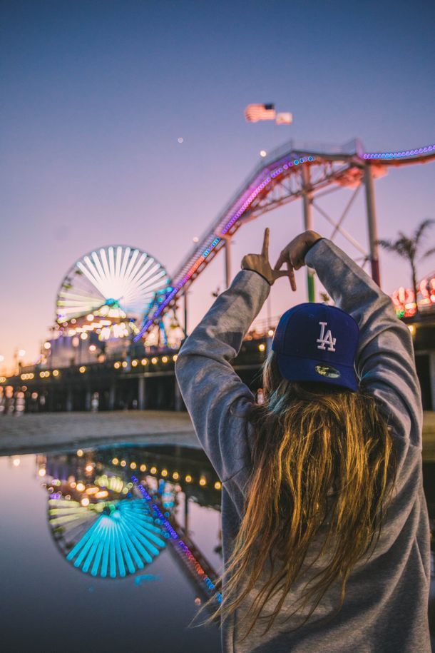 A woman is taking a picture of a roller coaster at Santa Moncia  piere.