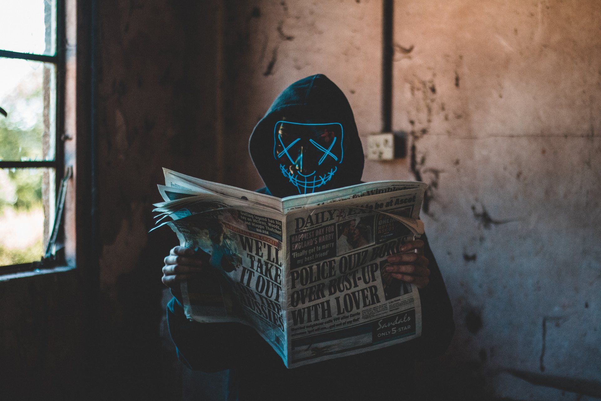 A person wearing a neon mask is reading a newspaper.