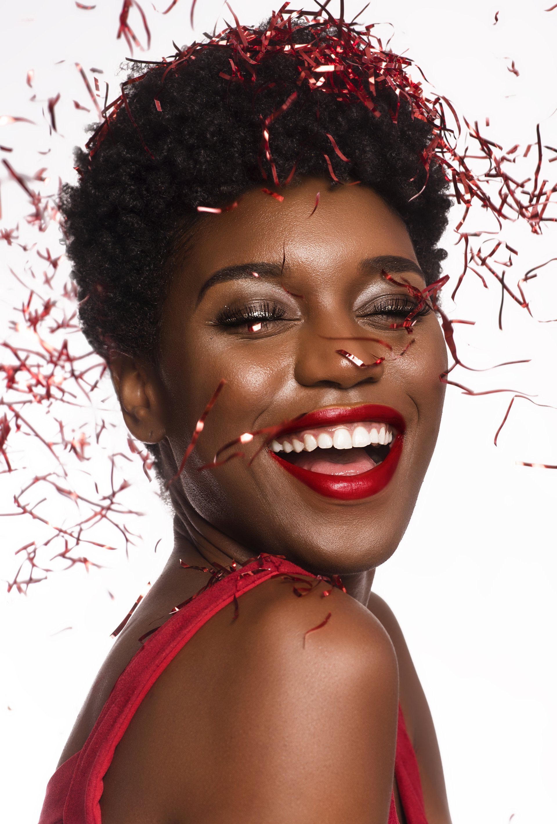A woman with red lipstick and confetti on her face is smiling.