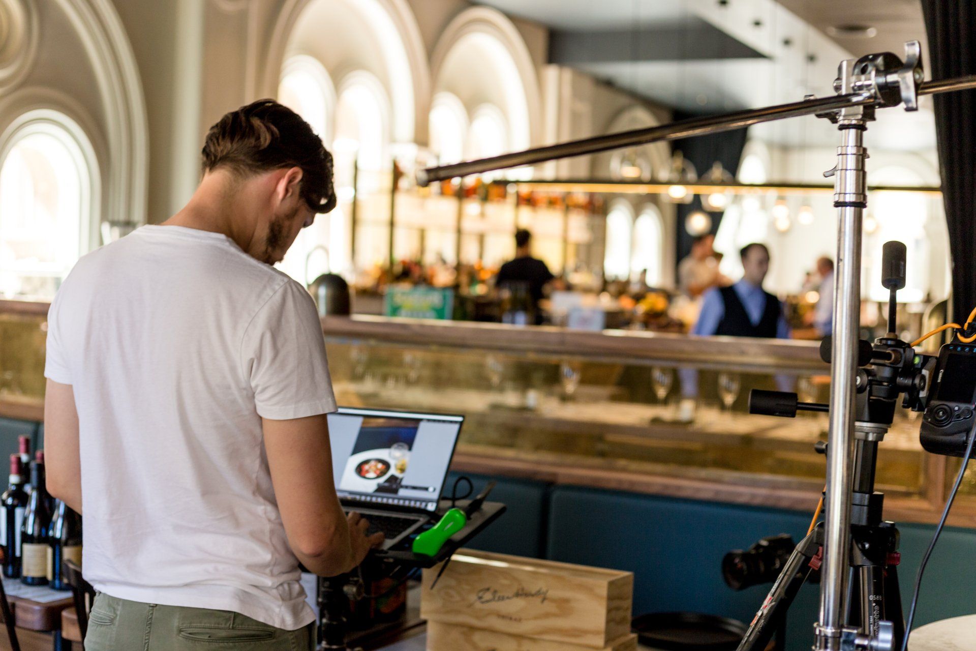 A man is standing in front of a laptop computer in a restaurant.