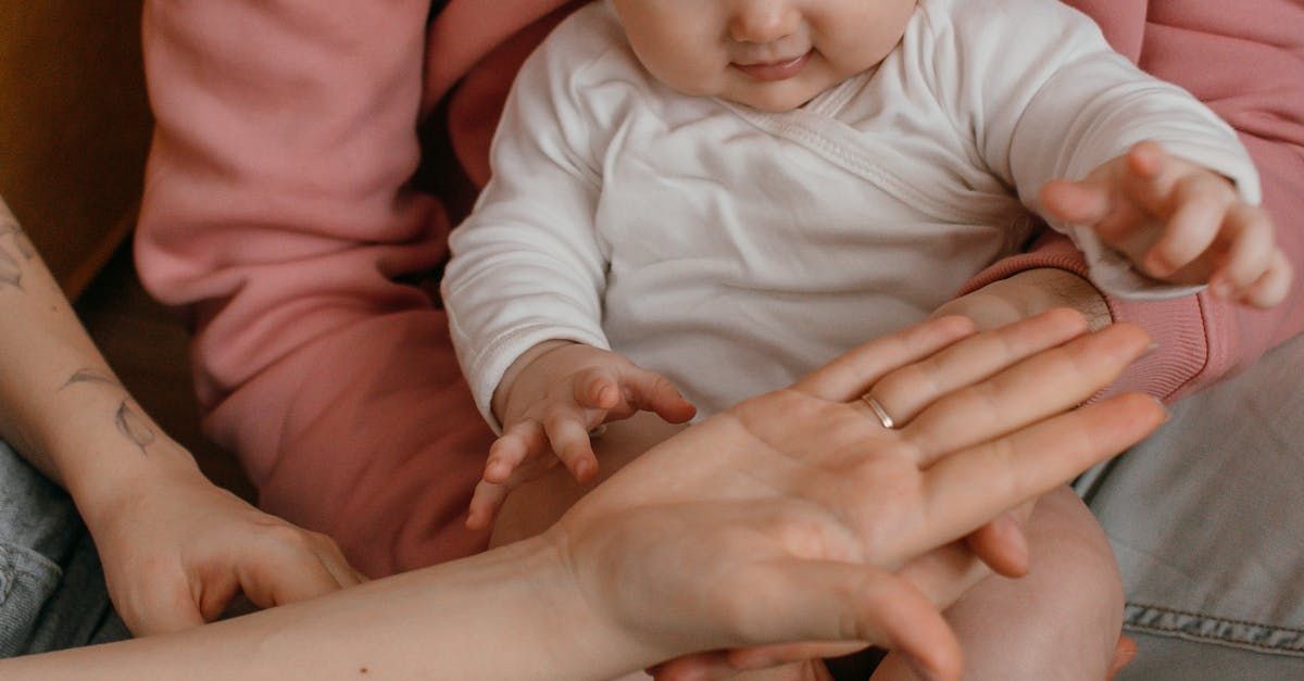 A baby is sitting on a woman 's lap and playing with her hands.