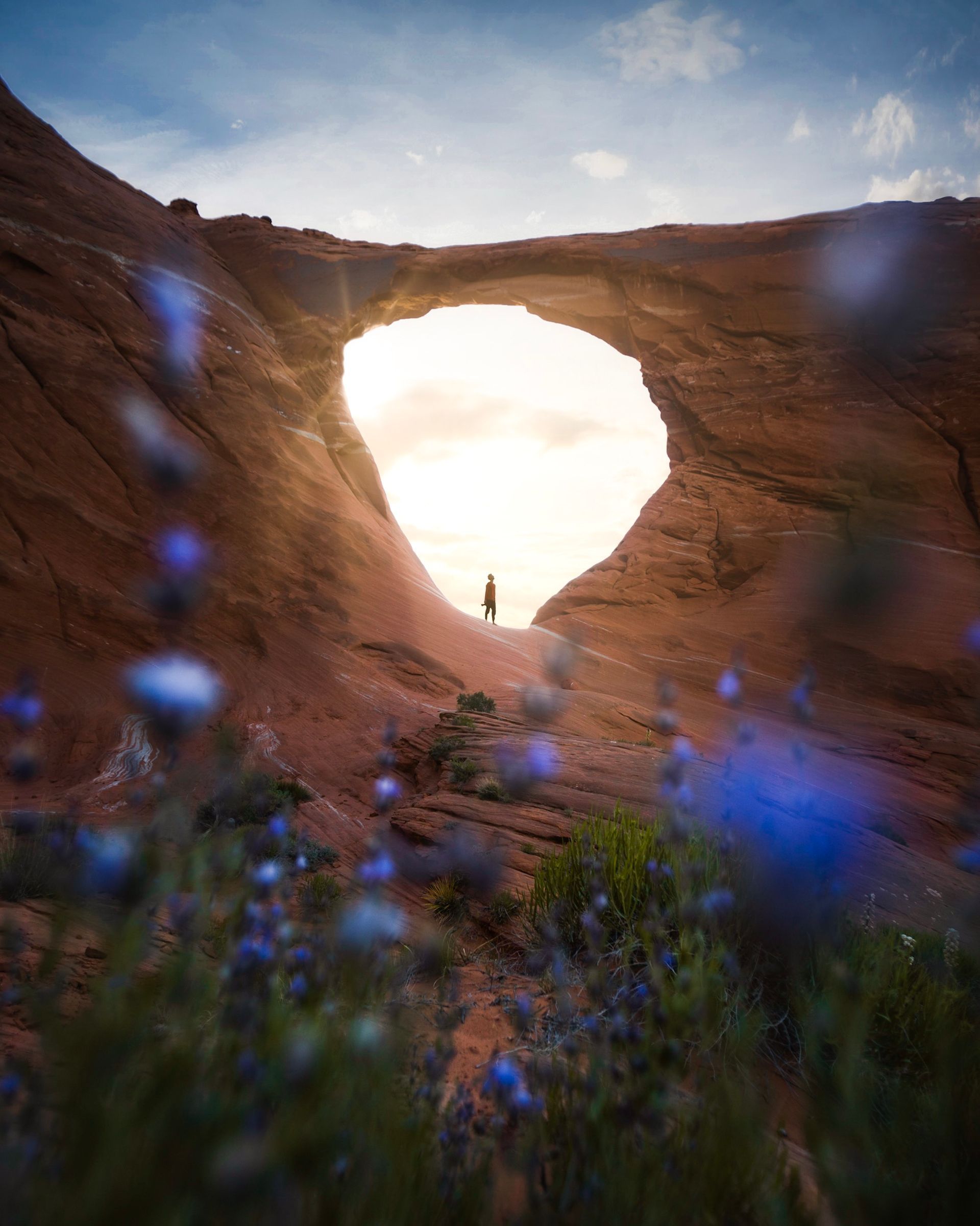 a person is standing in the middle of a canyon with the sun shining through the archway .