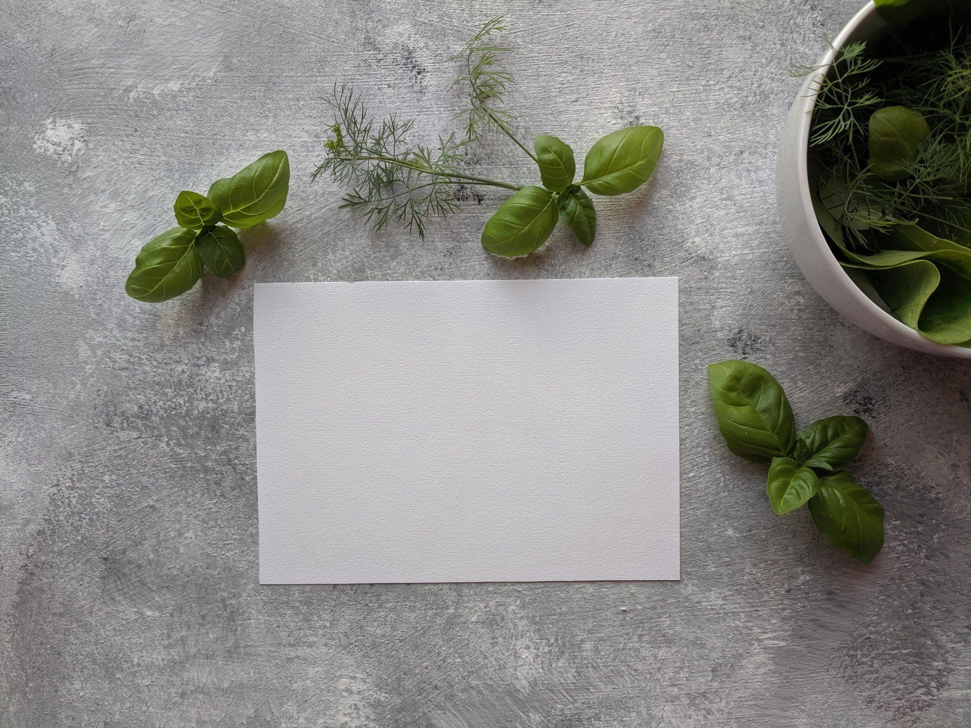 There is a bowl of herbs and a piece of paper on the table.