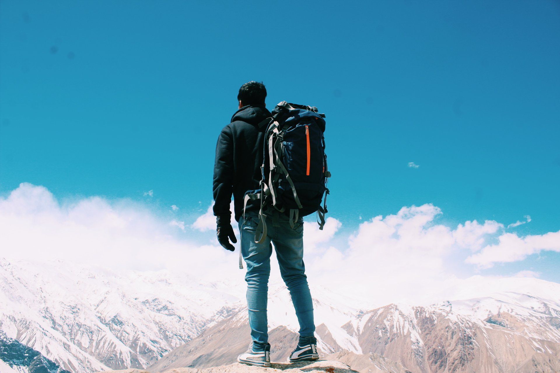 A man with a backpack is standing on top of a snowy mountain.