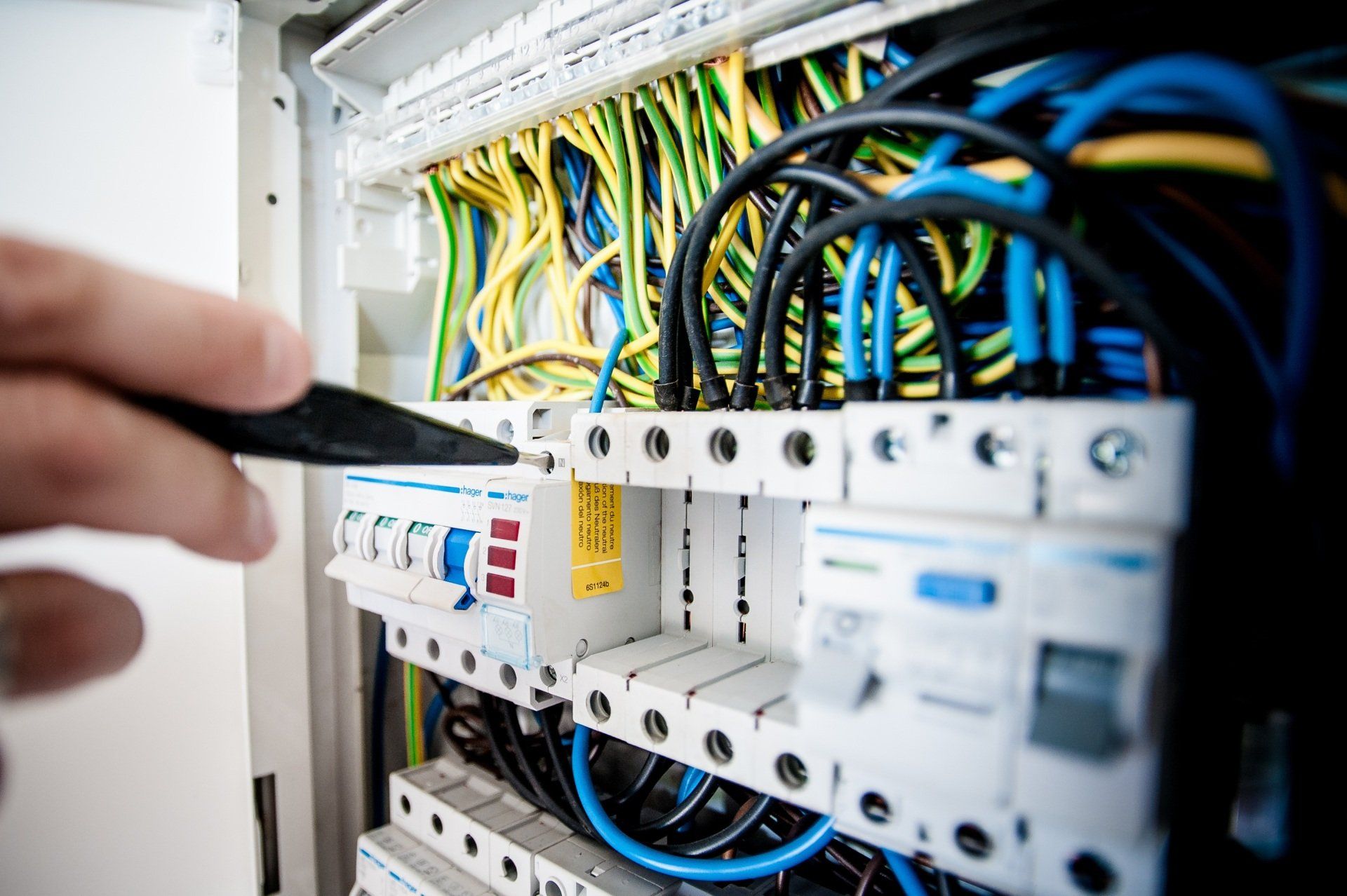 An electrician performing a test on an electrical panel, checking its protective shield and connections.
