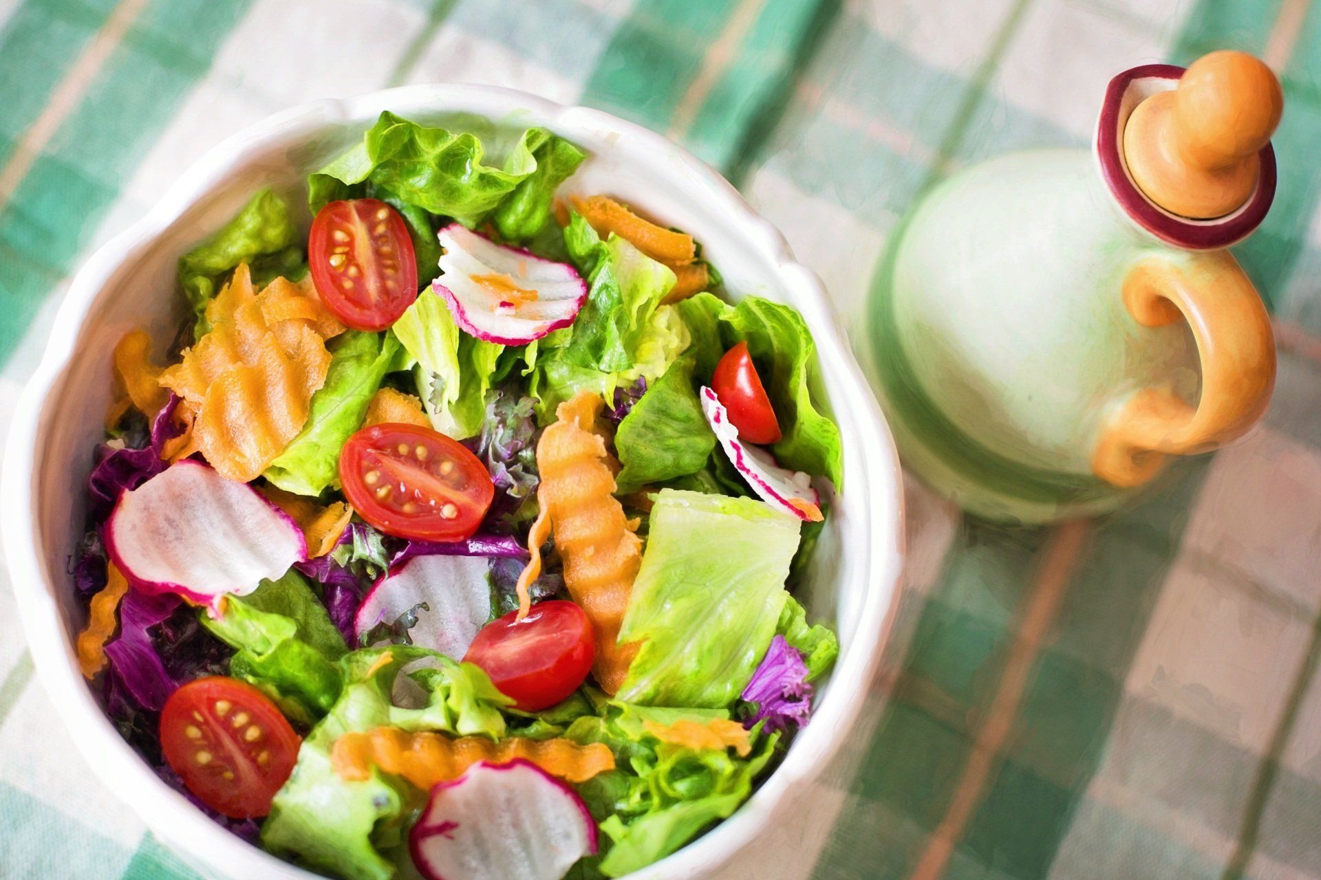 a bowl of salad with tomatoes , lettuce , carrots and radishes on a table .