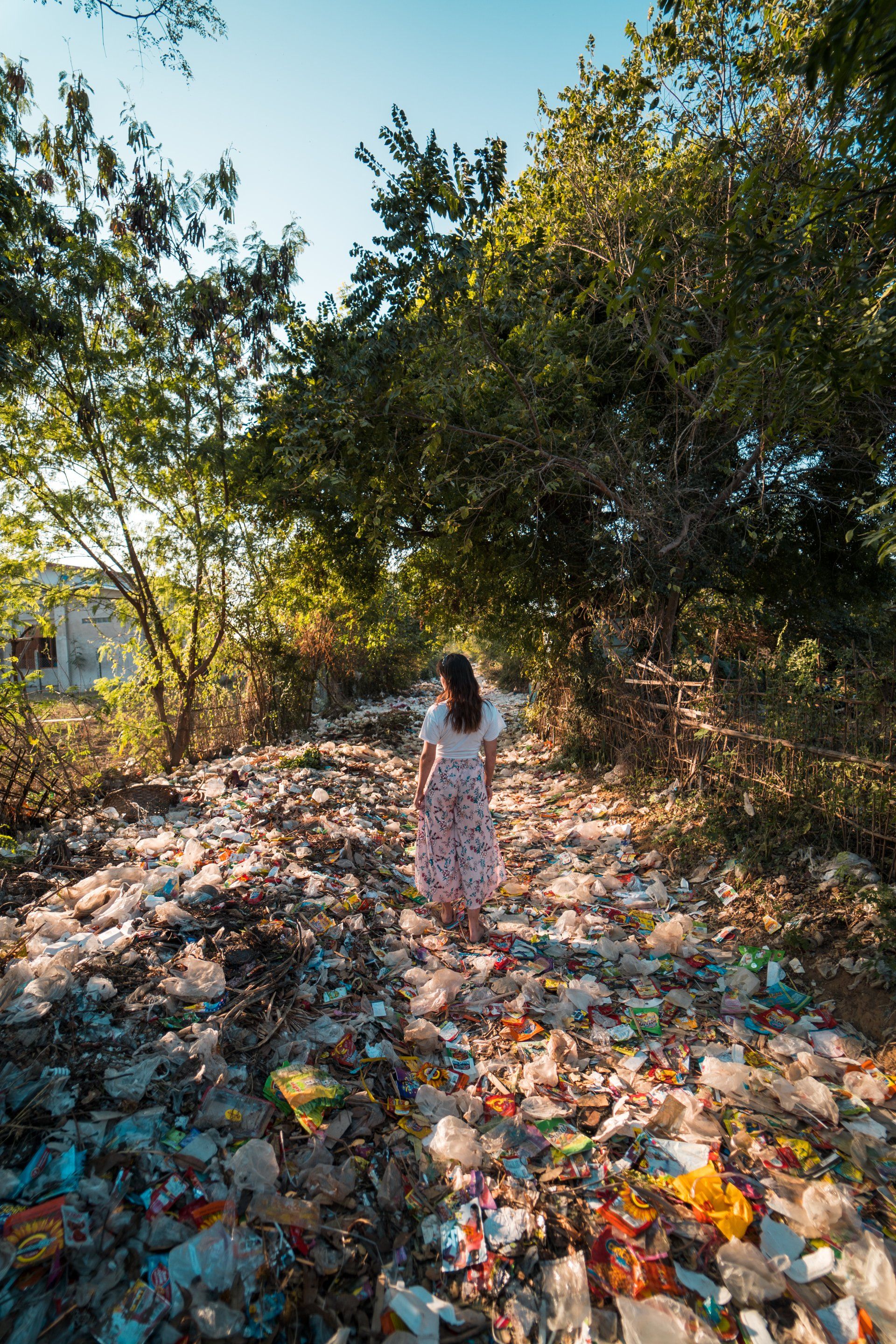 A woman is walking through a pile of trash in the woods.