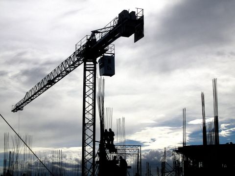 A construction crane is silhouetted against a cloudy sky