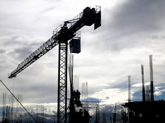 A construction crane is silhouetted against a cloudy sky