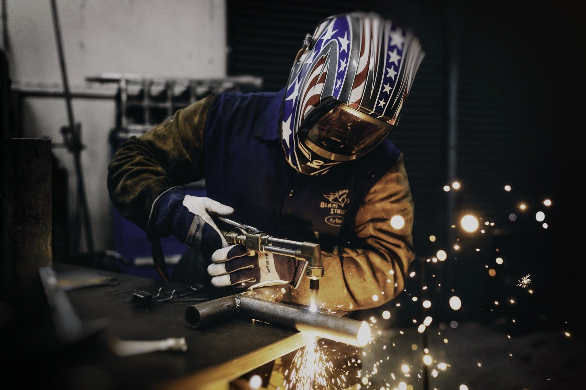 A man wearing a welding helmet meticulously welds metal pieces together on a table.